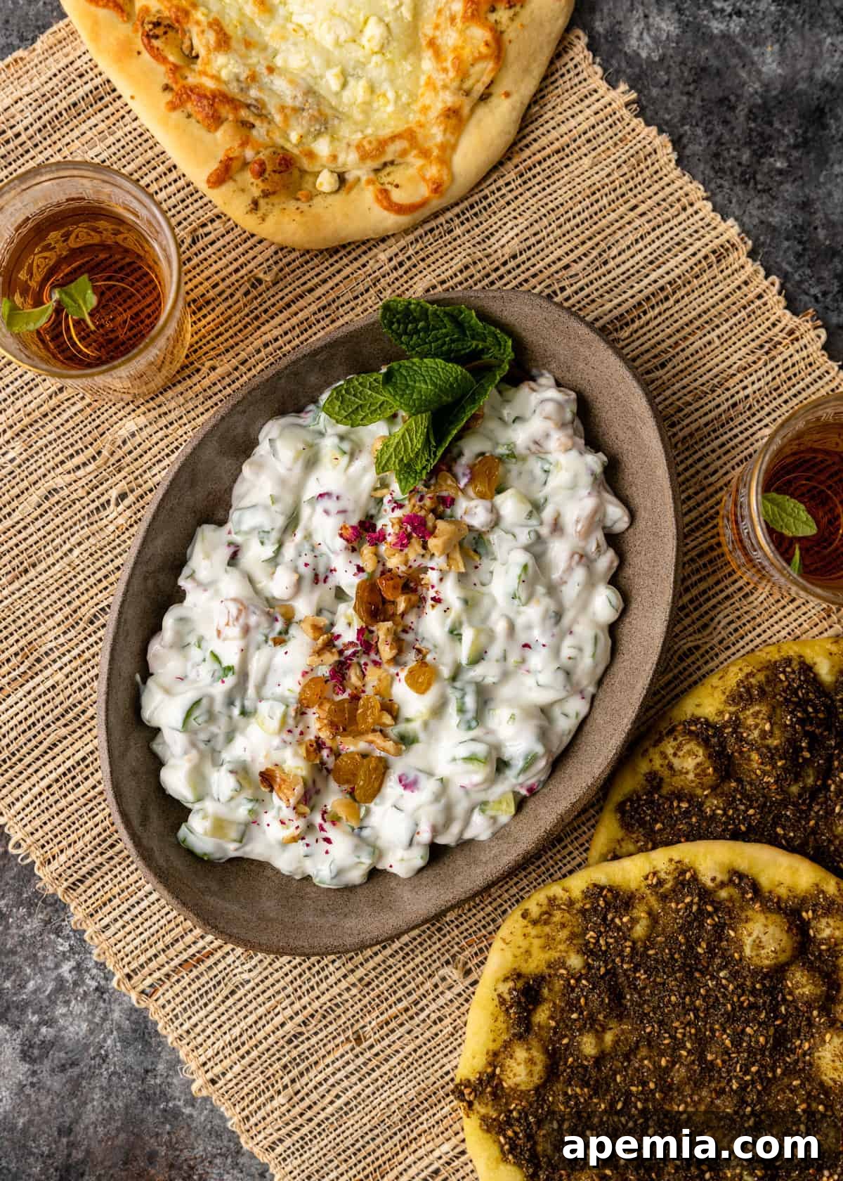 Refreshing Persian Mast O Khiar Cucumber Yogurt 3 overhead: Middle Eastern table with zaatar bread, persian cucumber yogurt dip, and glass of tea on woven placemat