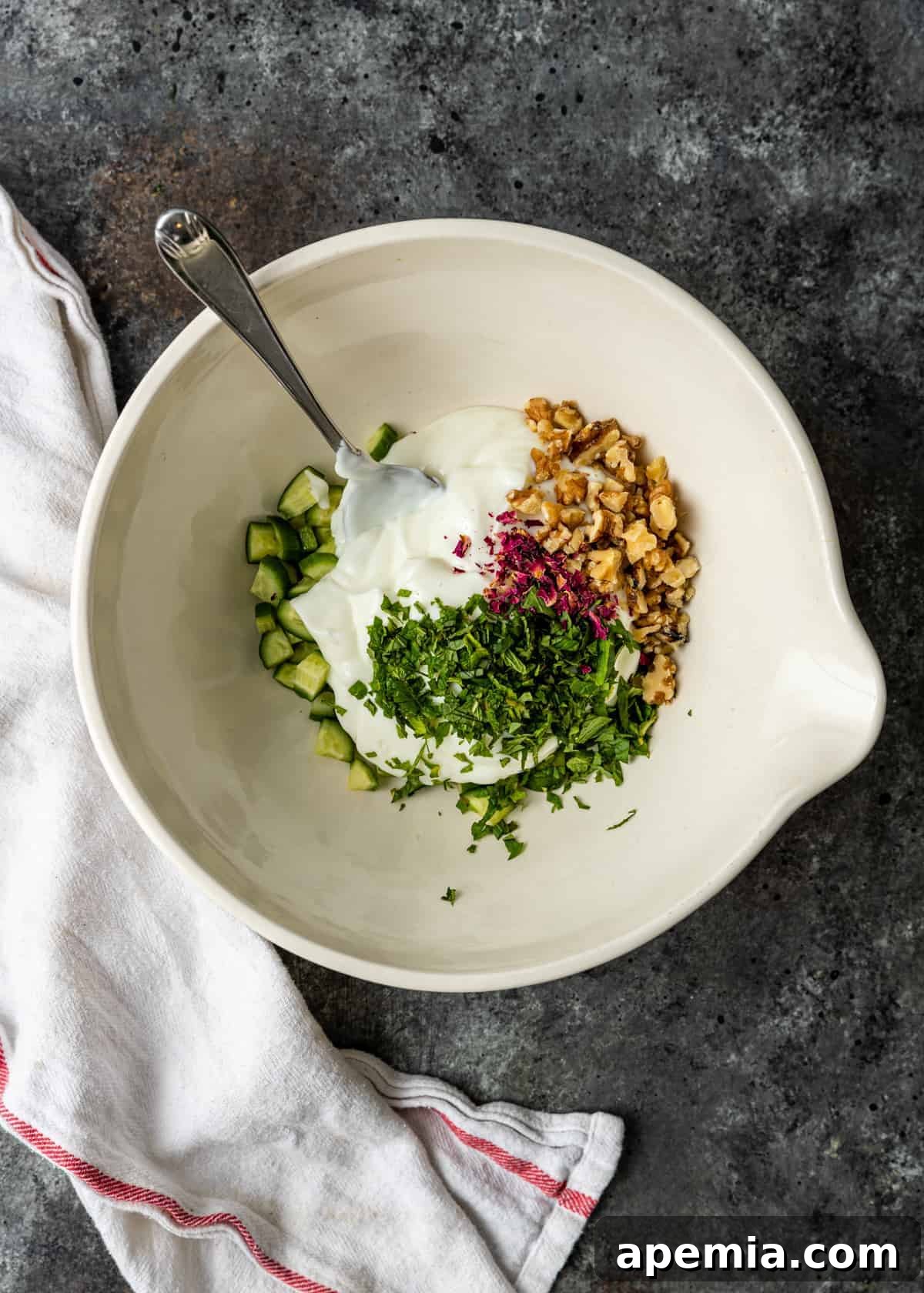 Refreshing Persian Mast O Khiar Cucumber Yogurt 4 overhead: diced Persian cucumbers, walnuts, rose petals and yoghurt in white bowl for salad