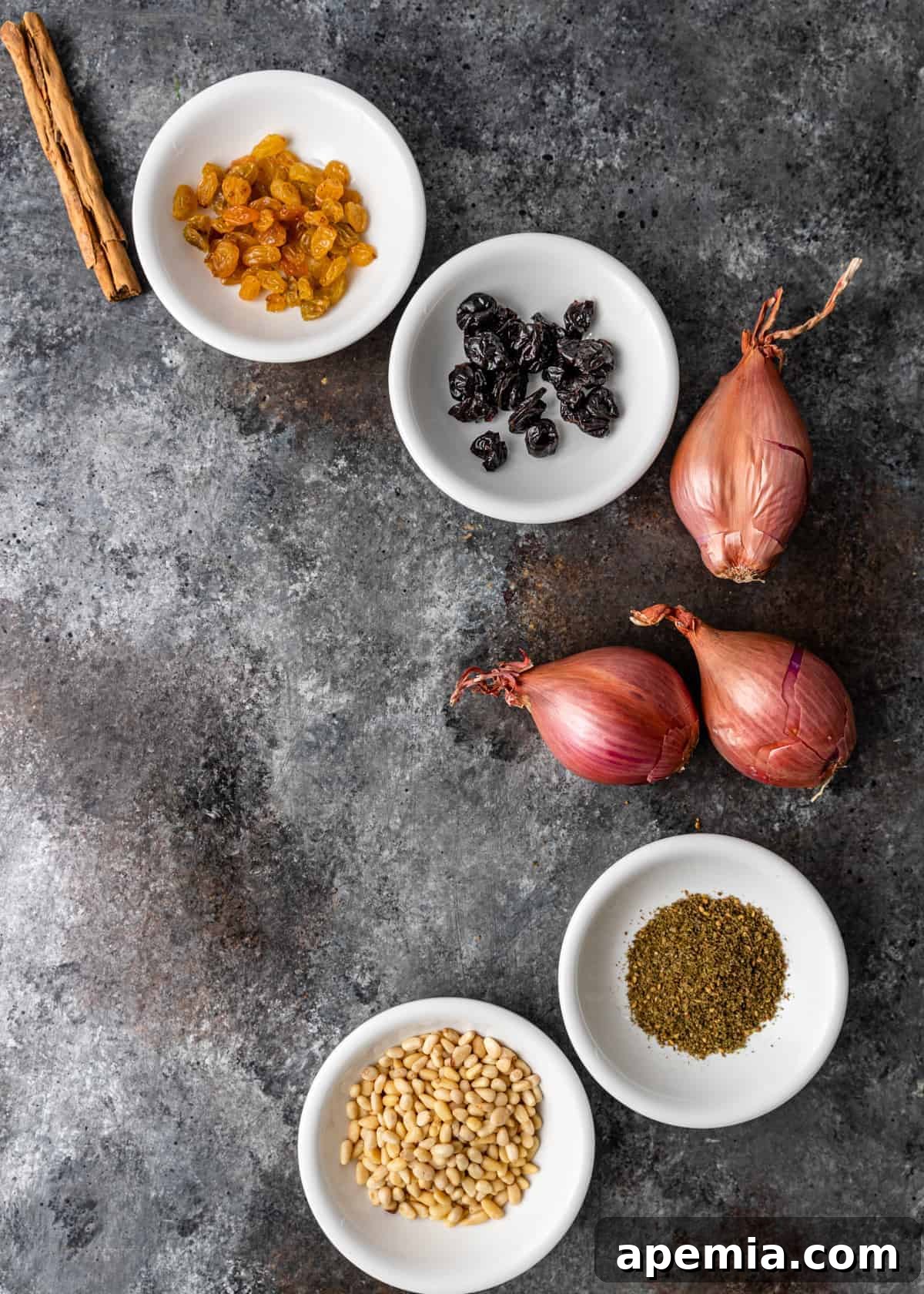 overhead: bowls of golden raisins, dried cherries, za'atar spice and pine nuts next to whole, 3unpeele d shallots
