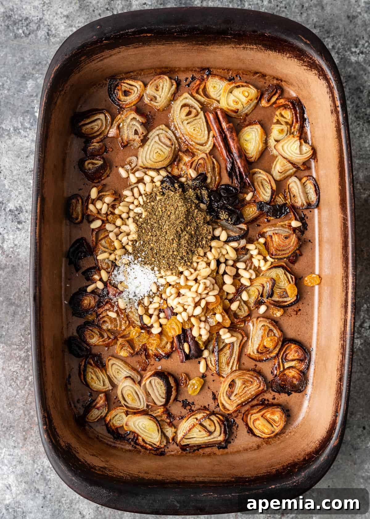 overhead: layer of Lebanese spices and shallot slices in bottom of casserole dish