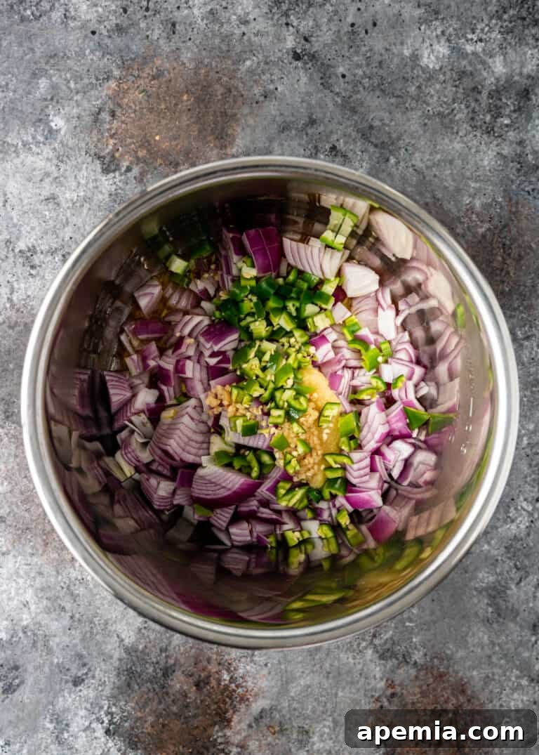 A pot filled with chopped raw red onion, green chili peppers, garlic, and seasonings, ready for cooking.