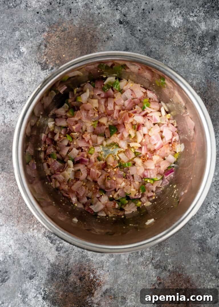 Overhead view of onion, garlic, and chile peppers sautéing in a large metal cooking pot, releasing their aromatic flavors.