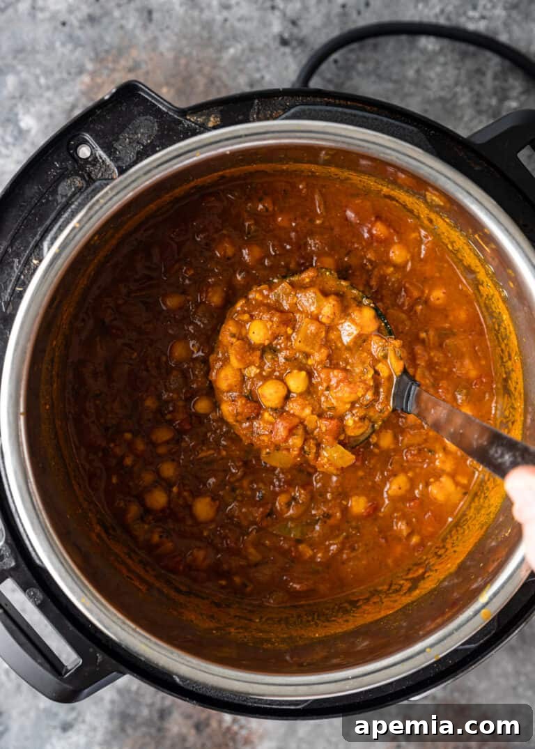 Overhead shot of Indian curry made with chickpeas being ladled from a pressure cooker, showcasing its rich texture.