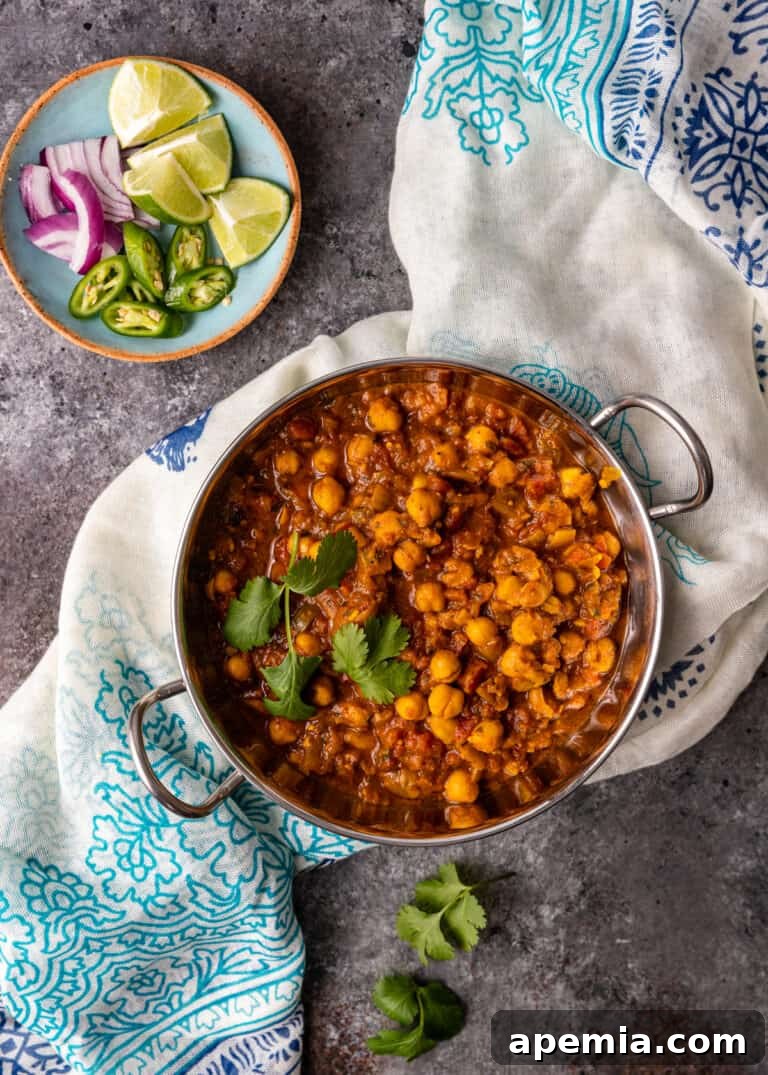 Overhead image of a serving dish filled with Instant Pot Chana Masala, placed on a table next to a plate of lime wedges, onion slices, and jalapeño.