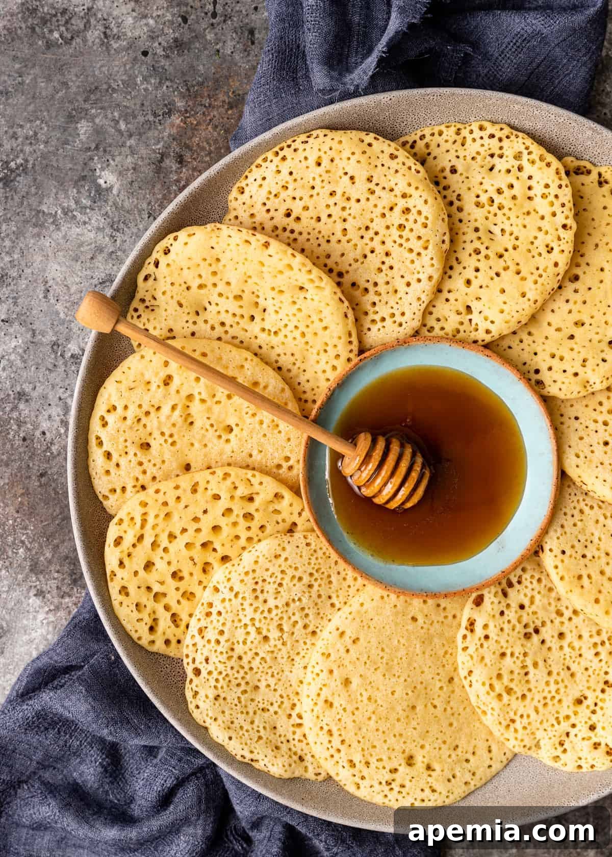 An overhead shot of a serving platter filled with numerous Baghrir pancakes arranged in a circular pattern around a central bowl of honey, ready to be enjoyed.