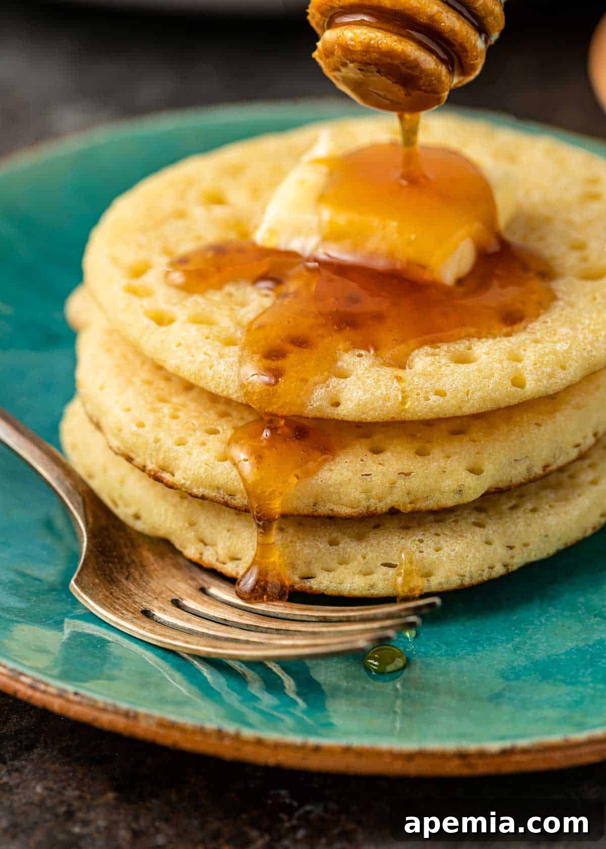 Close-up of golden honey being generously drizzled over a stack of fluffy Baghrir pancakes, emphasizing their porous texture perfect for absorbing toppings.