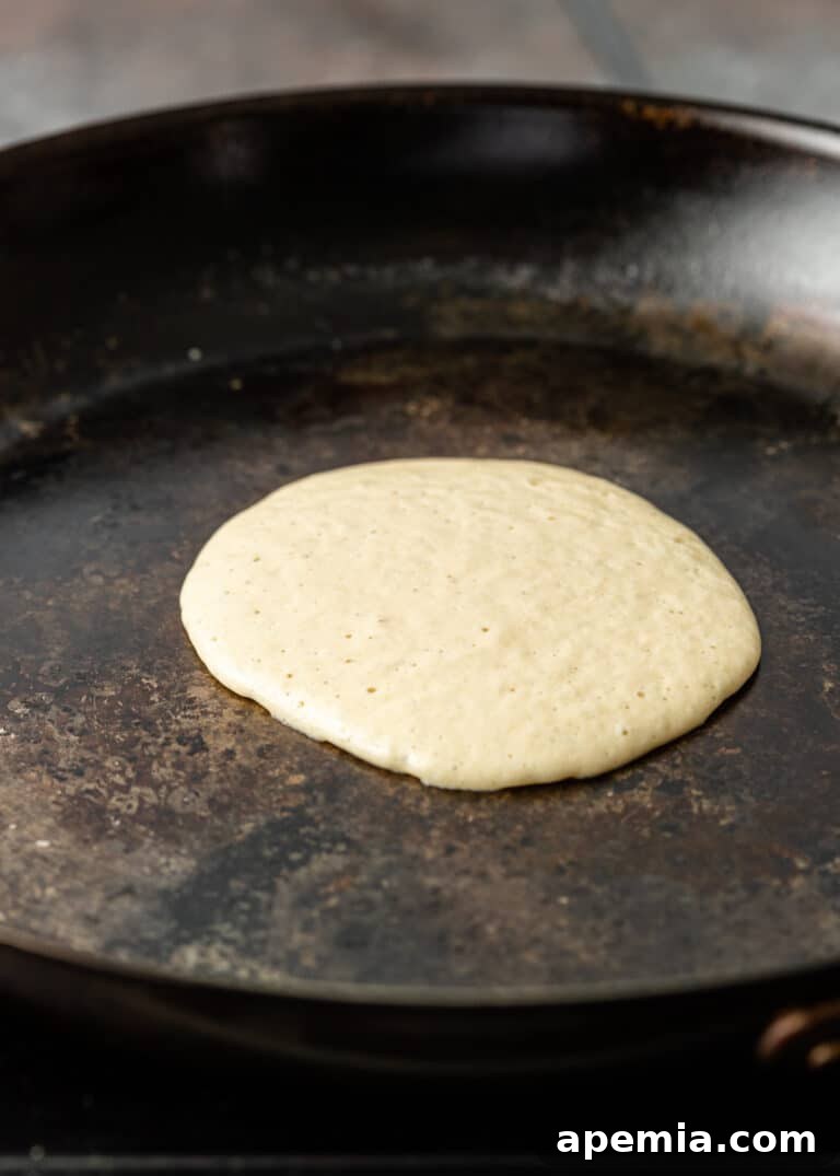 A close-up shot of Baghrir pancake batter cooking in a non-stick skillet, beginning to show small bubbles and a changing texture as it sets.