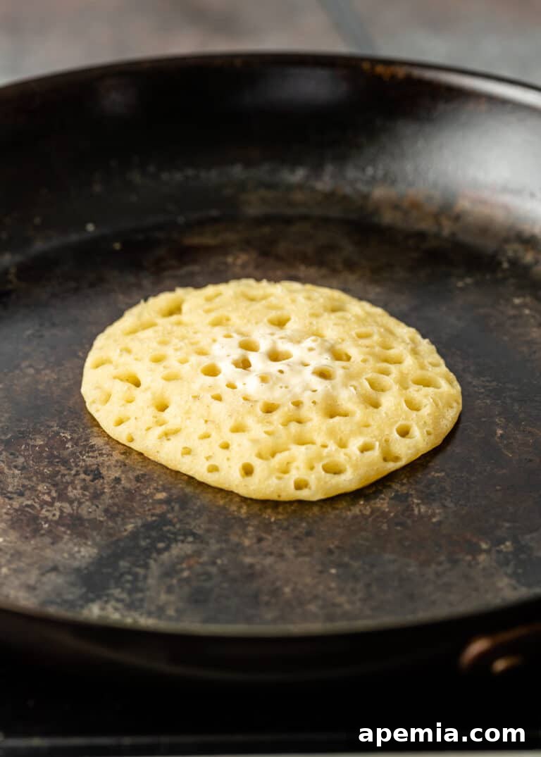 A single Baghrir pancake perfectly cooked in a skillet, its top dry and fully covered in tiny holes, with no need for flipping.