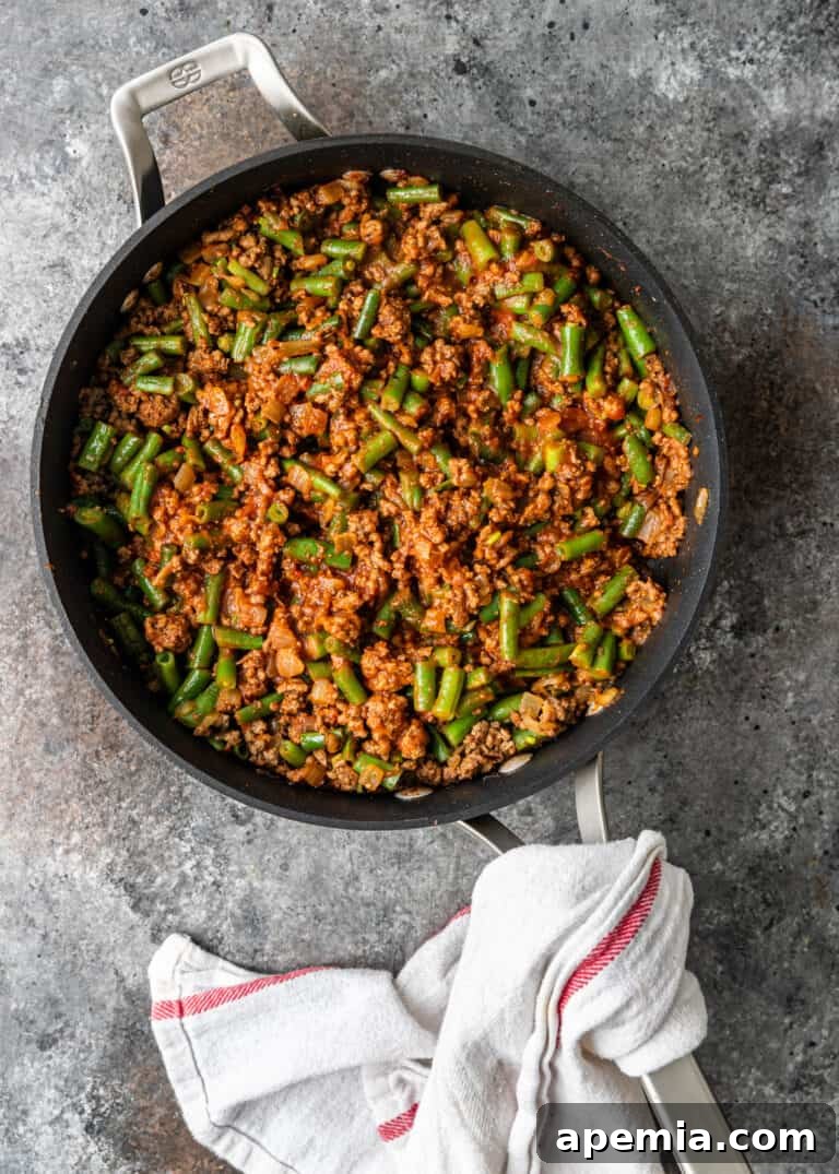 overhead process shot: ground beef with green beans in skillet