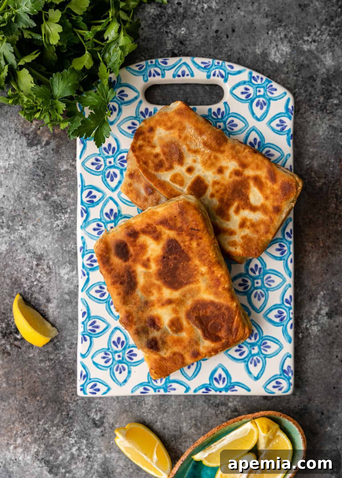 Overhead view of two Turkish stuffed flatbreads (Gozleme) on a decorative blue and white serving board, with lemon wedges on the side.
