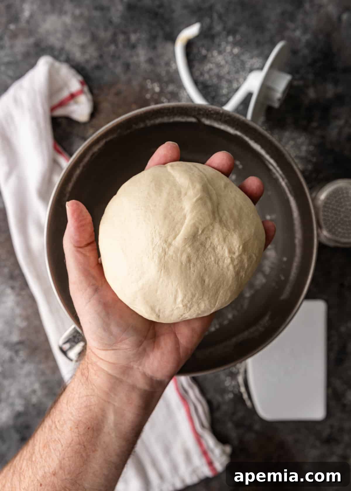 Overhead view of a hand holding a large ball of Gozleme dough, showcasing its pliable texture.
