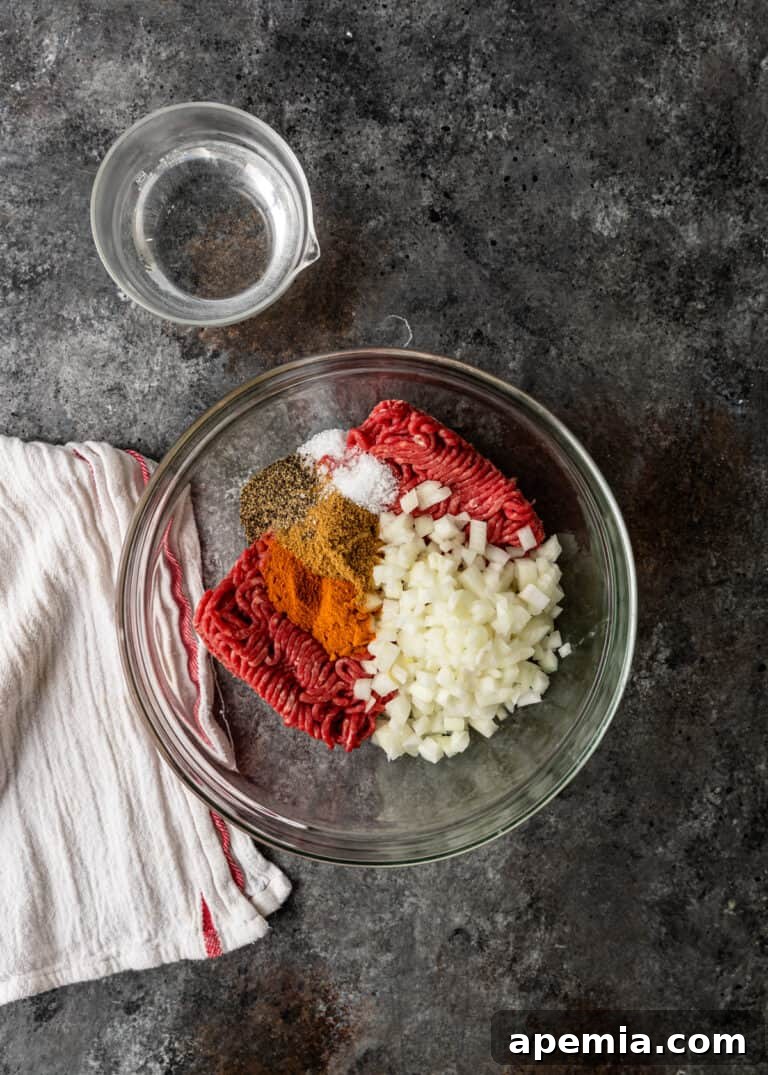 Overhead process shot: Raw ground beef in a glass mixing bowl with diced onion and Turkish spices.