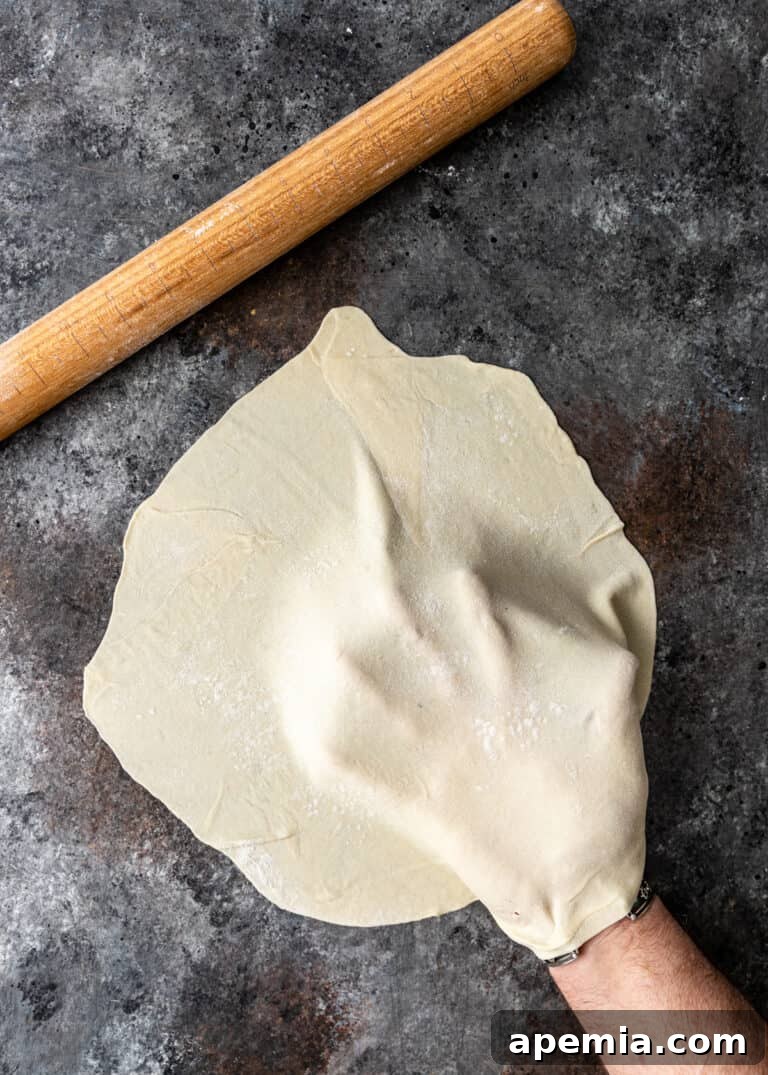 Overhead process shot: Man's hand holding a thin sheet of Turkish Gozleme dough.
