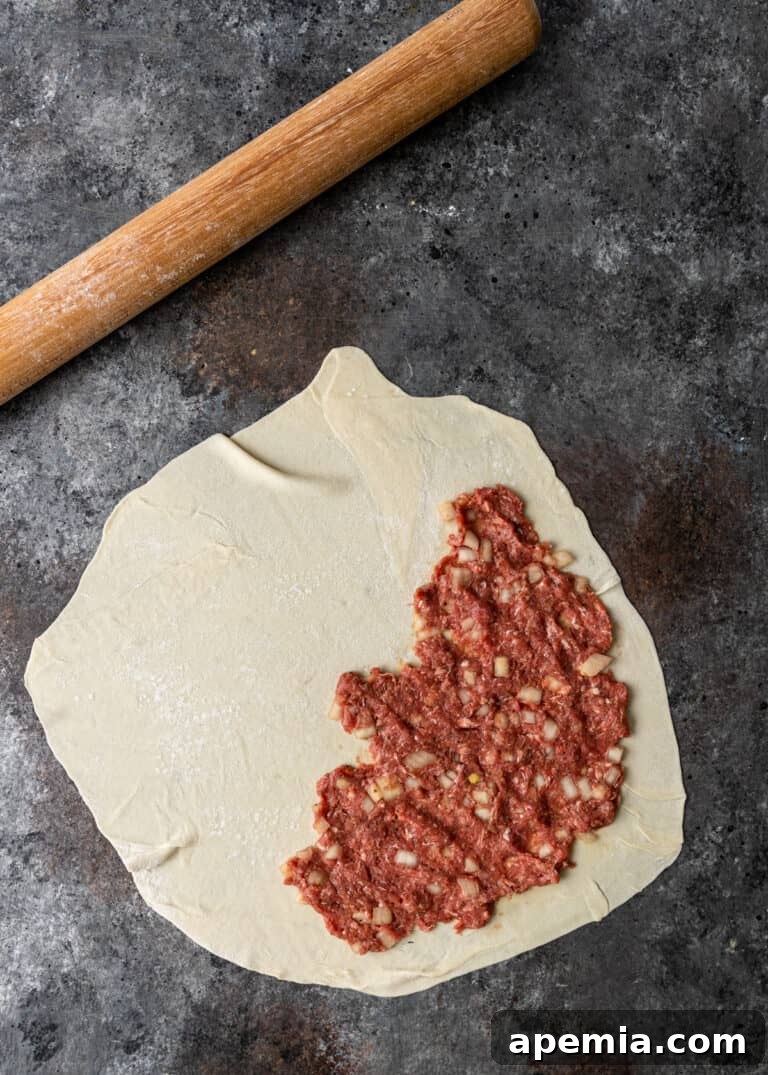 Overhead process shot: Circle of raw pastry dough topped with raw ground beef mixture.