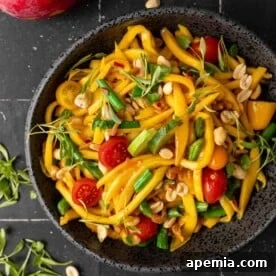 Overhead view of a bowl of vibrant Asian fruit and vegetable salad, featuring mango, green beans, and tomatoes.