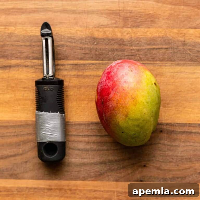 Whole fresh mango on a cutting board with a vegetable peeler, ready for preparation.