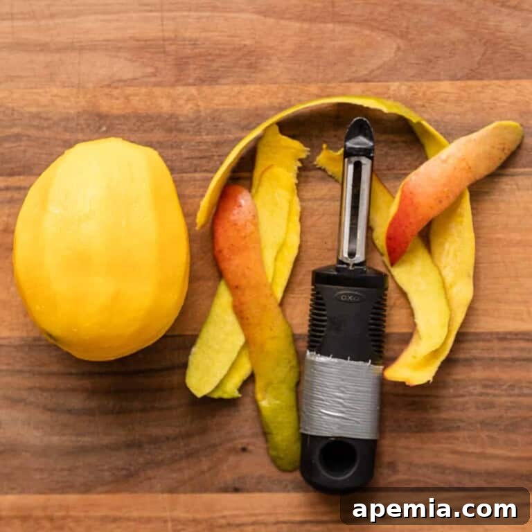 Peeled mango and a vegetable peeler on a wooden cutting board, illustrating the initial step of mango preparation.