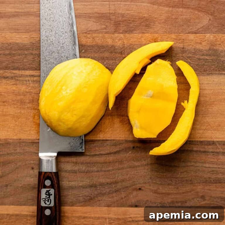 Overhead view of a mango cut away from its pit on a wooden cutting board with a chef's knife, showing the successful removal of the fruit flesh.