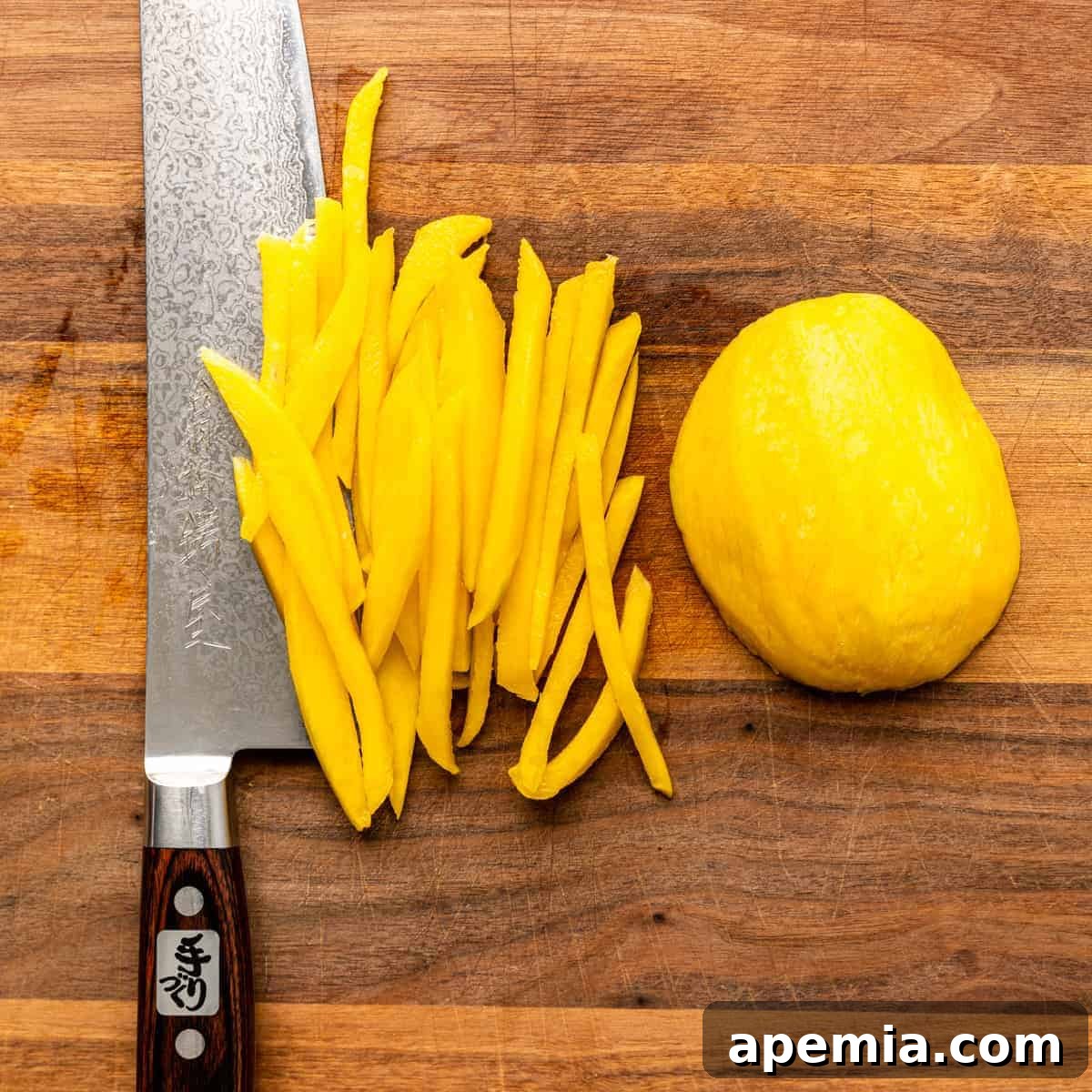 Overhead view of perfectly julienned strips of green mango alongside a large Chef's knife on a cutting board, ready for the salad.
