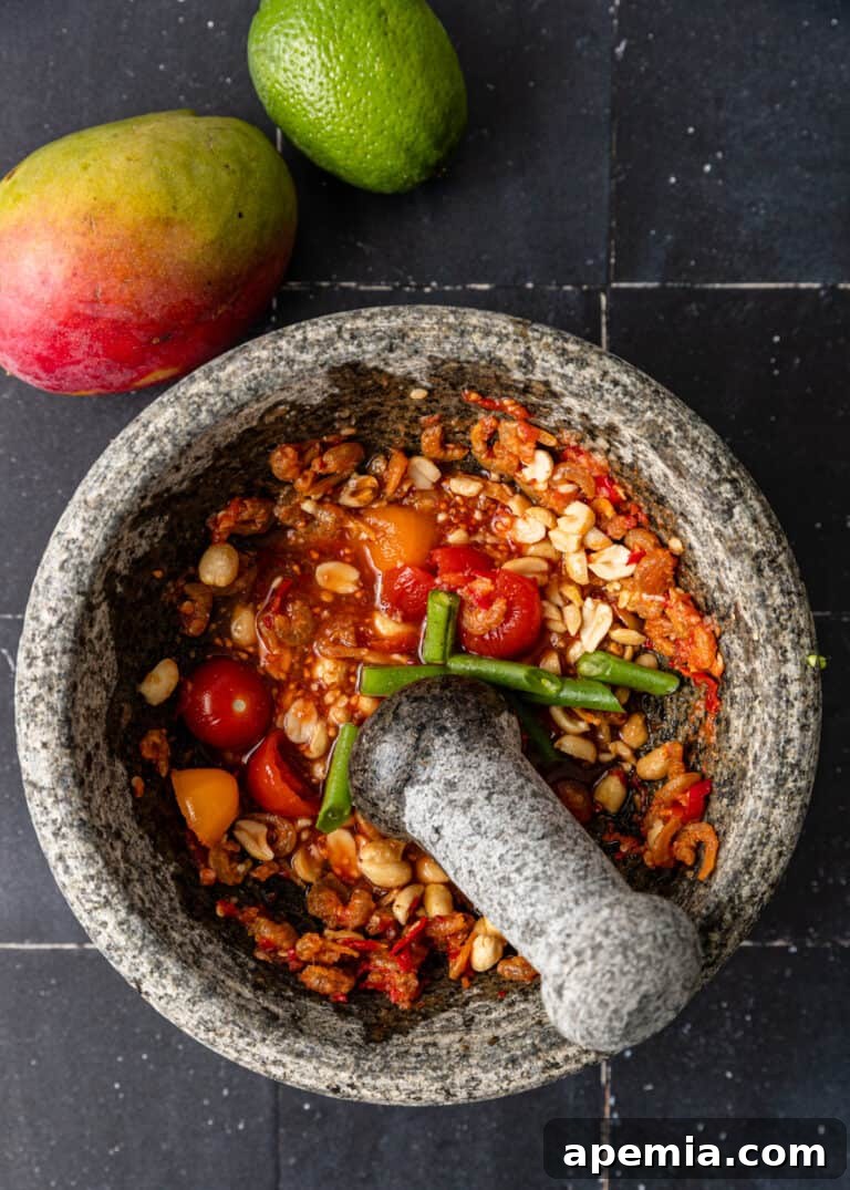 Hands using a mortar and pestle to crush red chiles and garlic, showing the traditional method for making the salad paste.
