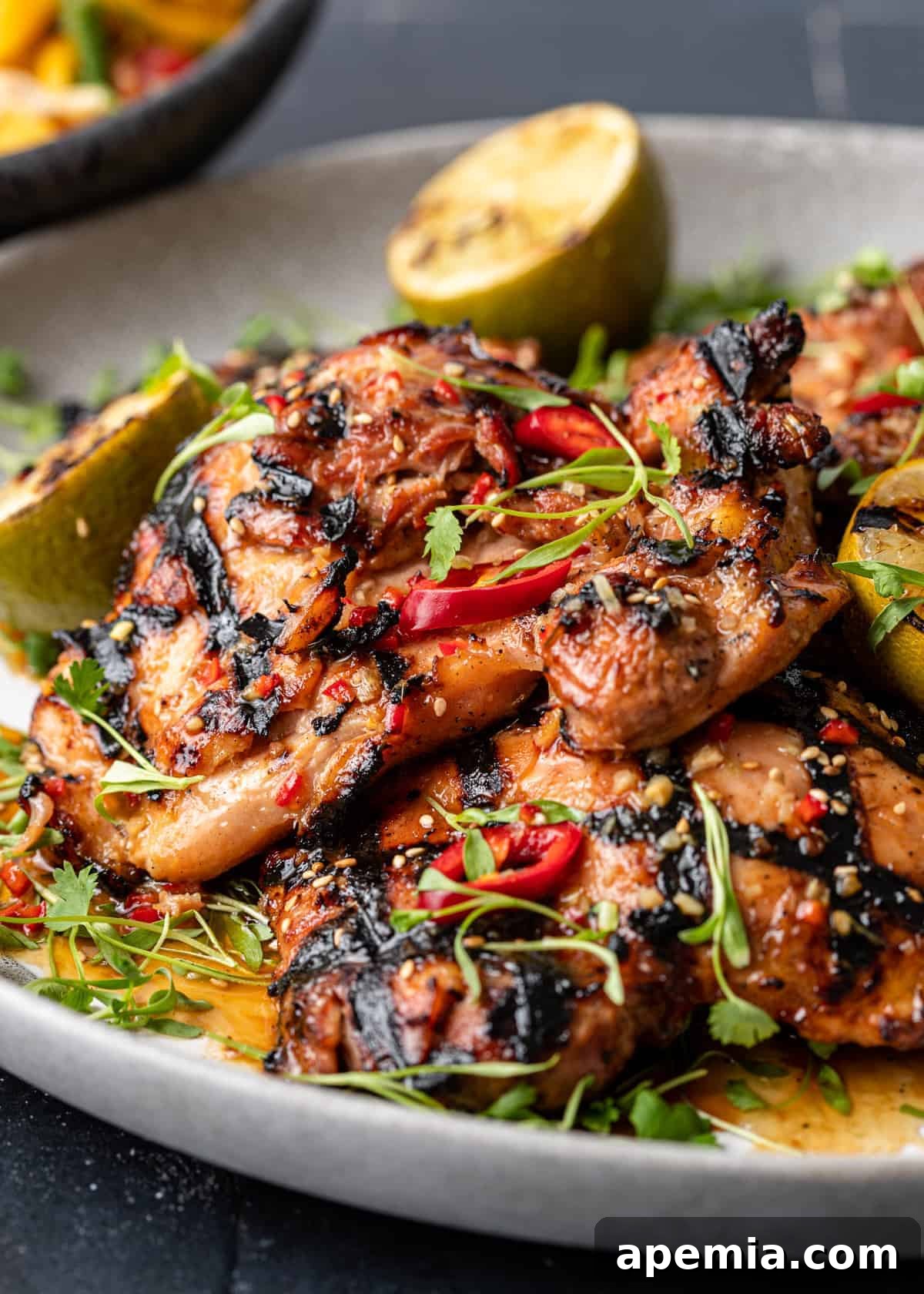 closeup: grilled gai yang chicken on round serving platter garnished with red chili peppers and lemongrass
