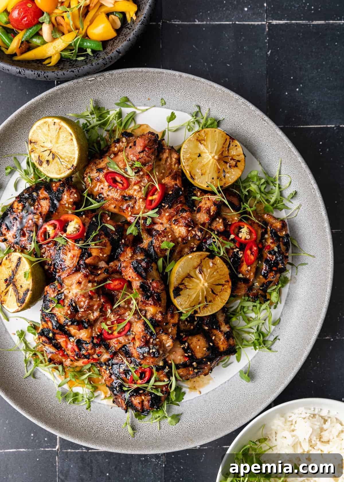 overhead: my Thai grilled chicken recipe on white serving platter with grilled limes and microgreens