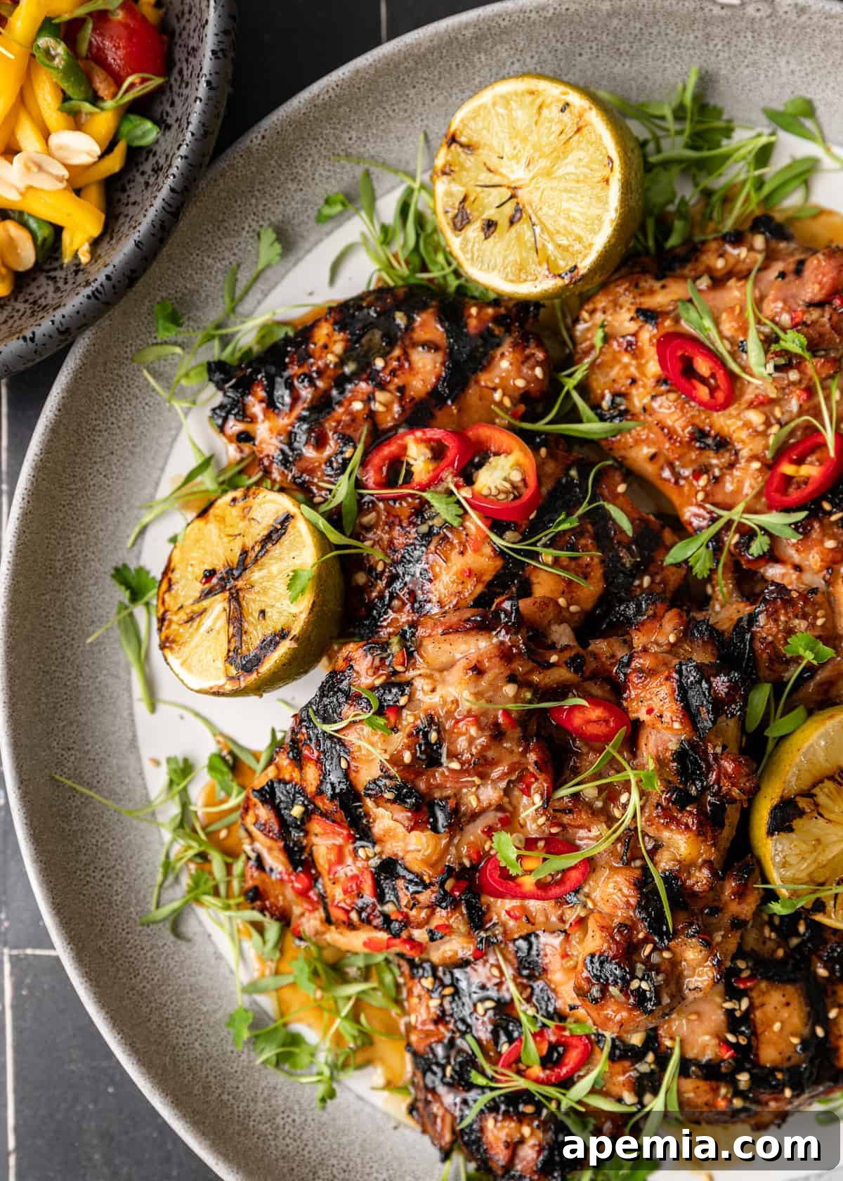 overhead: my Thai chicken recipe on round serving platter with grilled lime halves and red jalapeno