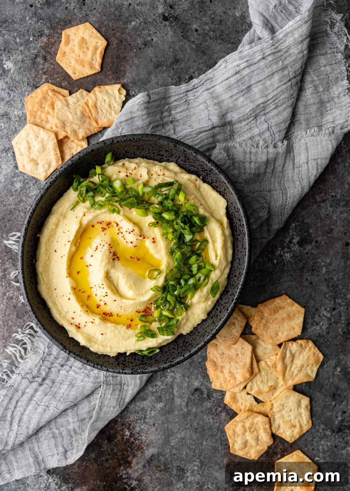 overhead: creamy skordalia served in black bowl surrounded by hexagon shaped crackers