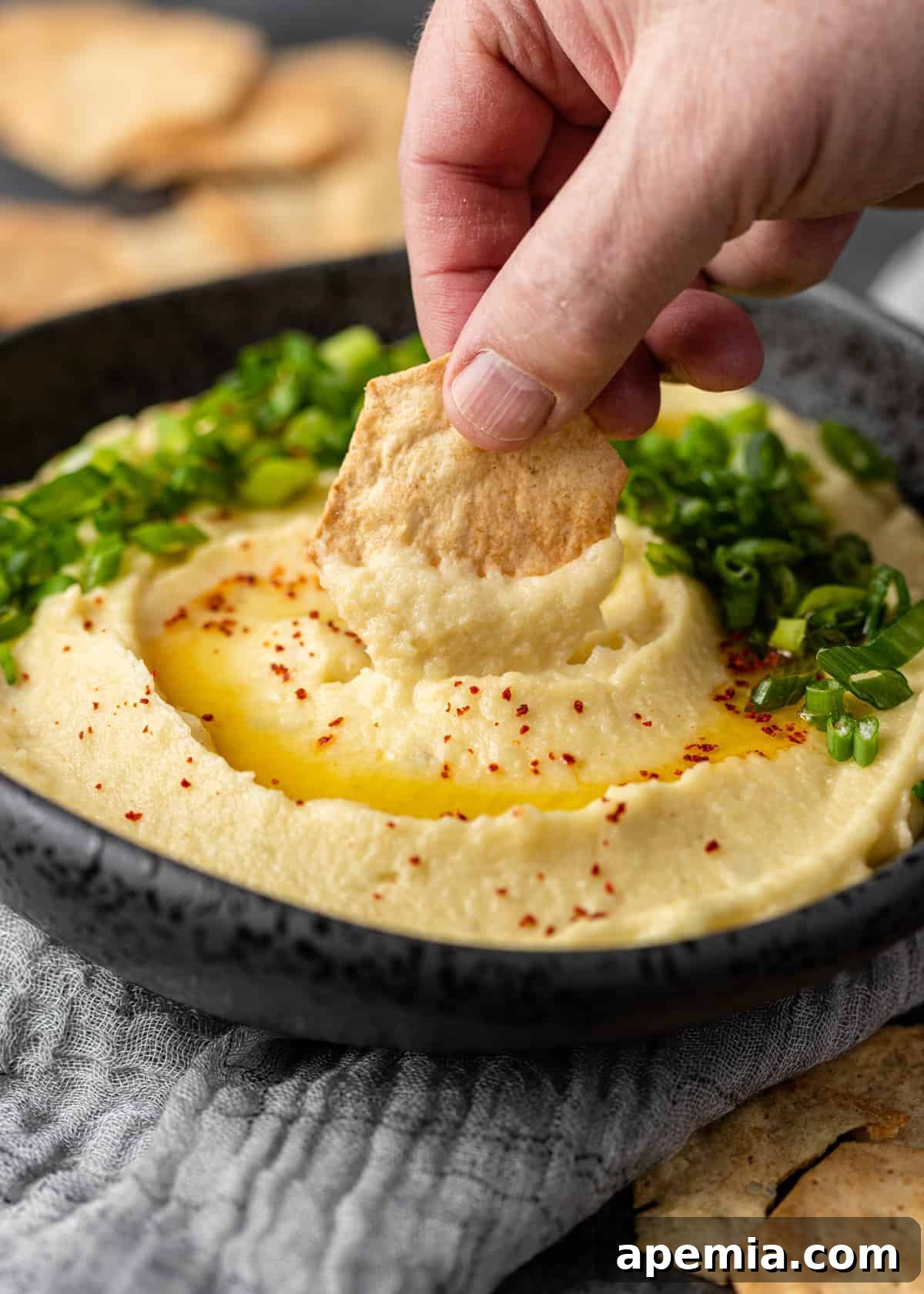 man's hand dipping cracker into bowl of Greek potato and garlic dip