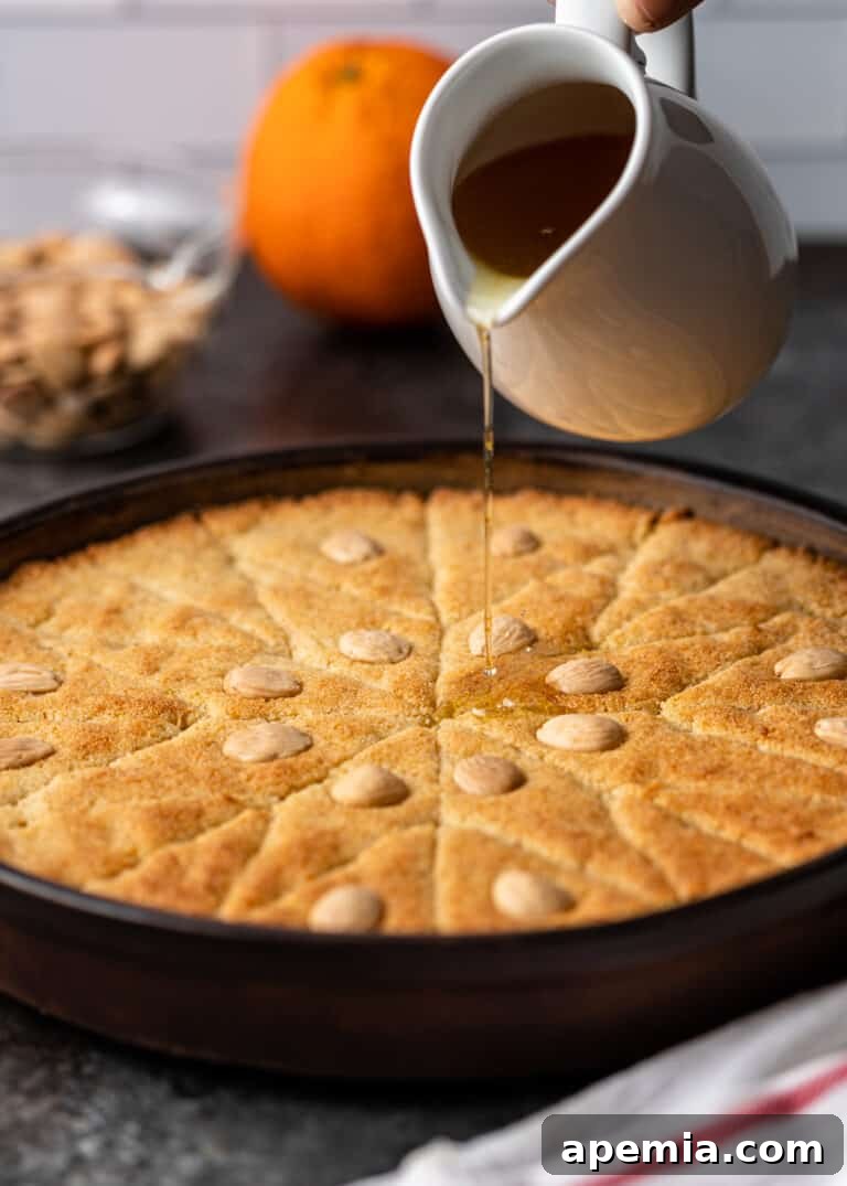 Egyptian Basbousa Golden Semolina Bliss 10 Side view of a white pitcher gently pouring fragrant orange cake glaze over the warm, freshly baked Basbousa cake.