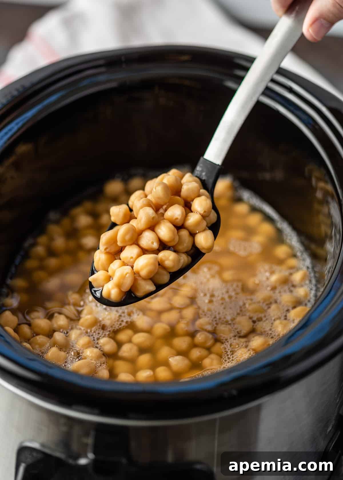 Garbanzo beans on a serving spoon above a slow cooker, showcasing the ease of batch cooking