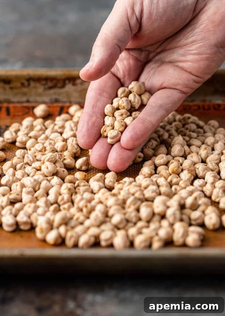 Man's hand sorting dried chickpeas on a sheet pan, showing the meticulous first step of preparation