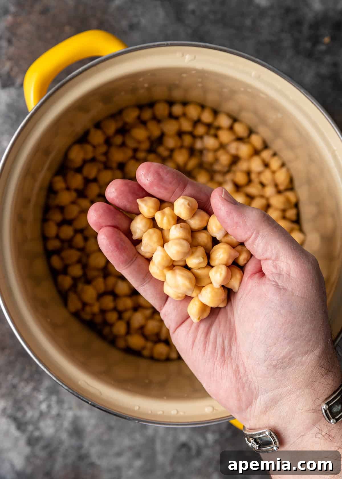 Man holding a handful of cooked chickpeas above a yellow pot, demonstrating successful preparation