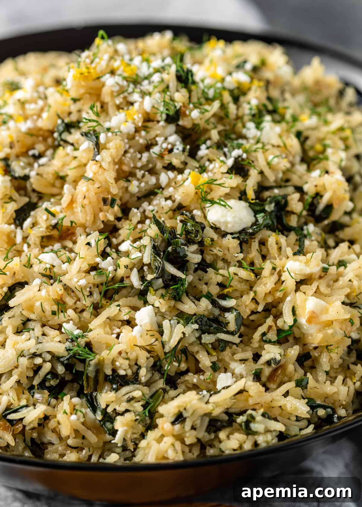 A close-up view of a bowl of Spanakorizo, showcasing long-grain rice mixed with vibrant spinach, crumbled feta cheese, and garnished with fresh lemon wedges and Greek seasoning.