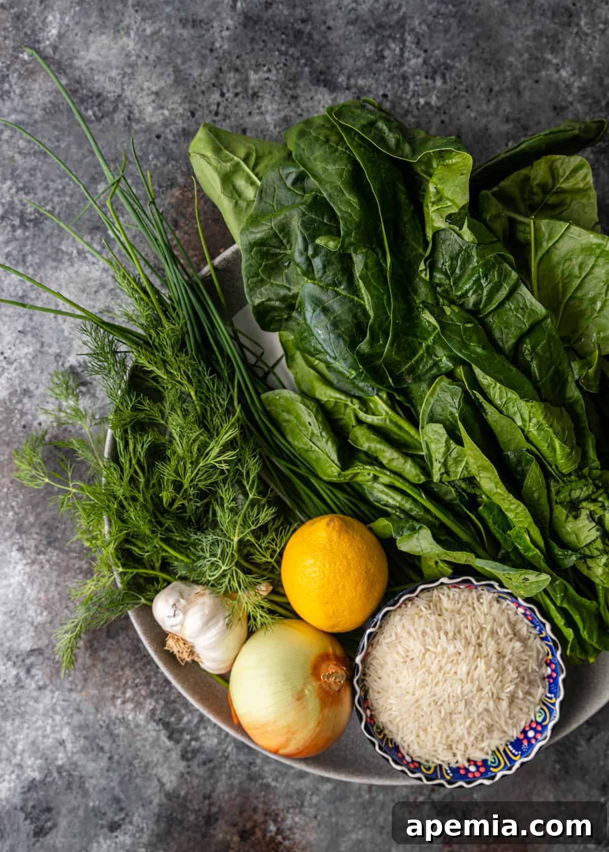 A collection of fresh ingredients laid out, including vibrant spinach leaves, whole garlic cloves, a bright lemon, and grains of rice, ready to be prepared for Spanakorizo.