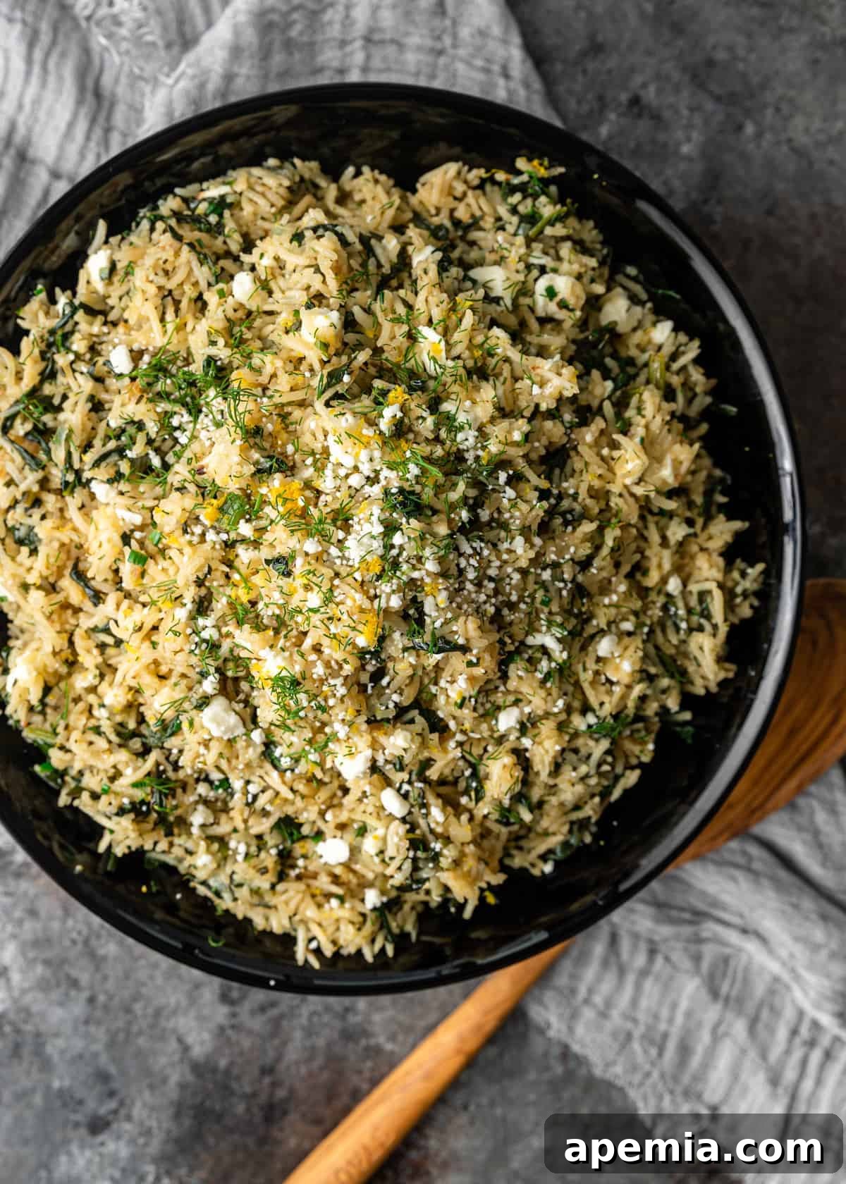 An overhead shot of a black bowl filled with perfectly cooked Spanakorizo, garnished with fresh dill, lemon wedges, and crumbled feta cheese, ready to be enjoyed.