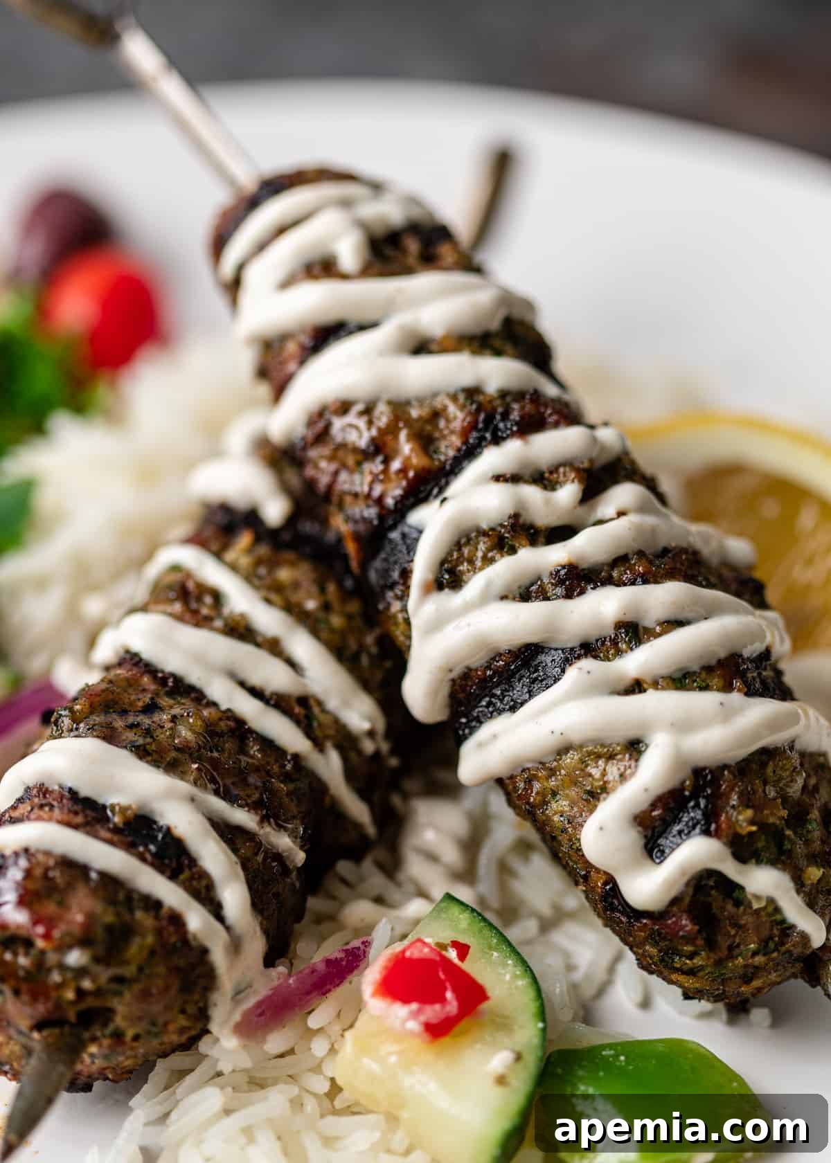 Two perfectly grilled ground beef kefta skewers, artfully drizzled with a creamy tahini yogurt sauce, highlighting the delicious contrast of textures and flavors.