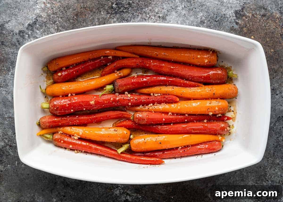 Bright orange and red heirloom carrots arranged neatly in a white rectangular baking dish, ready to be marinated and served.