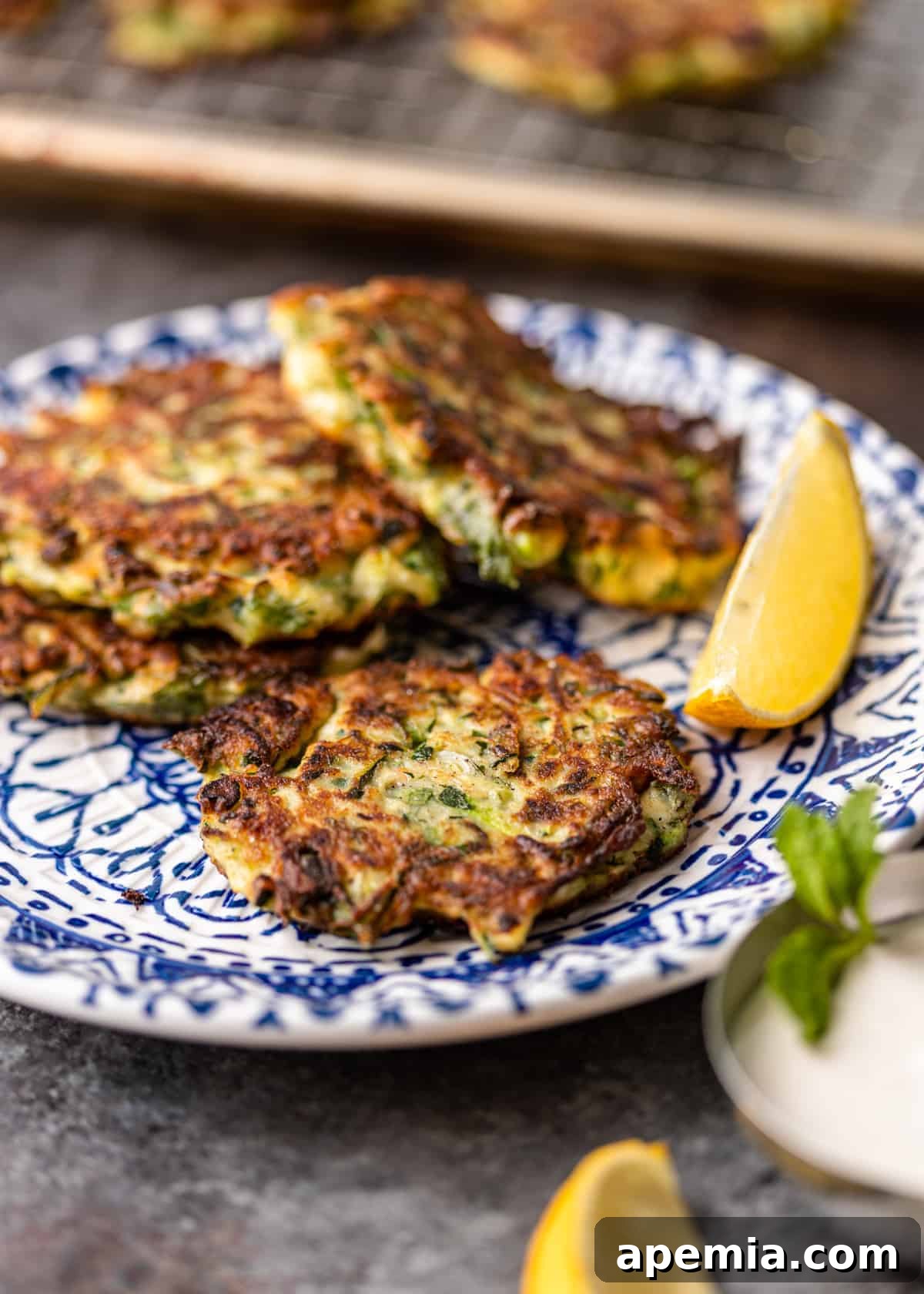 4 Greek zucchini pancakes on small blue and white plate with lemon wedge