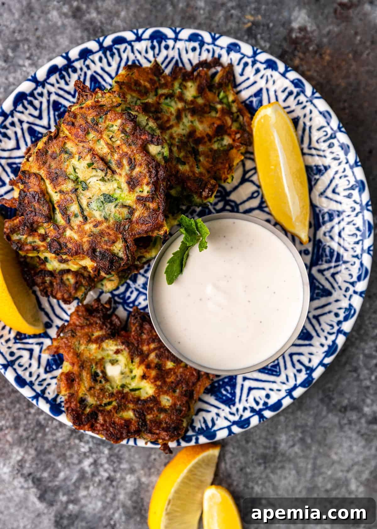 overhead image: crispy fried shredded zucchini patties on blue and white plate with cup of mint yogurt sauce
