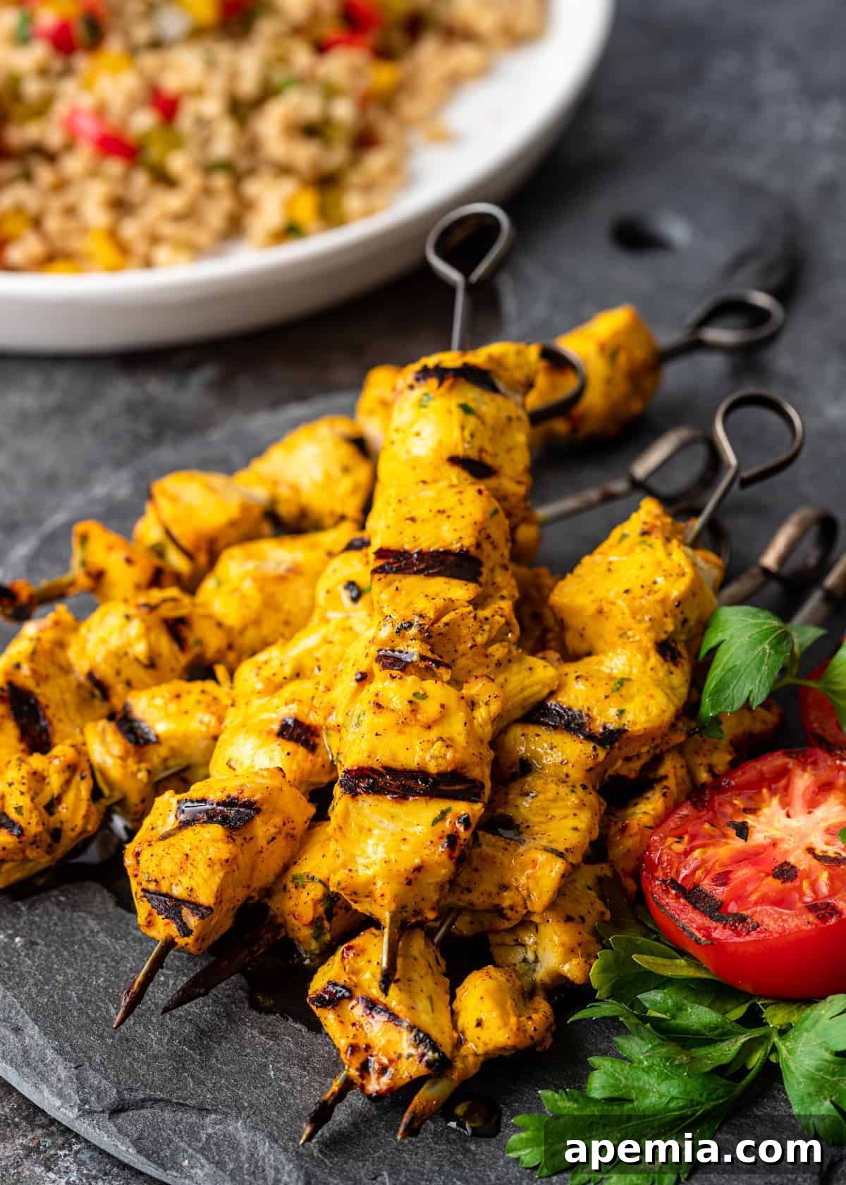 Close-up of Persian chicken kabobs showcasing the rich, vibrant color of saffron marinade, threaded onto metal skewers alongside grilled tomatoes and fresh herbs, ready for serving.