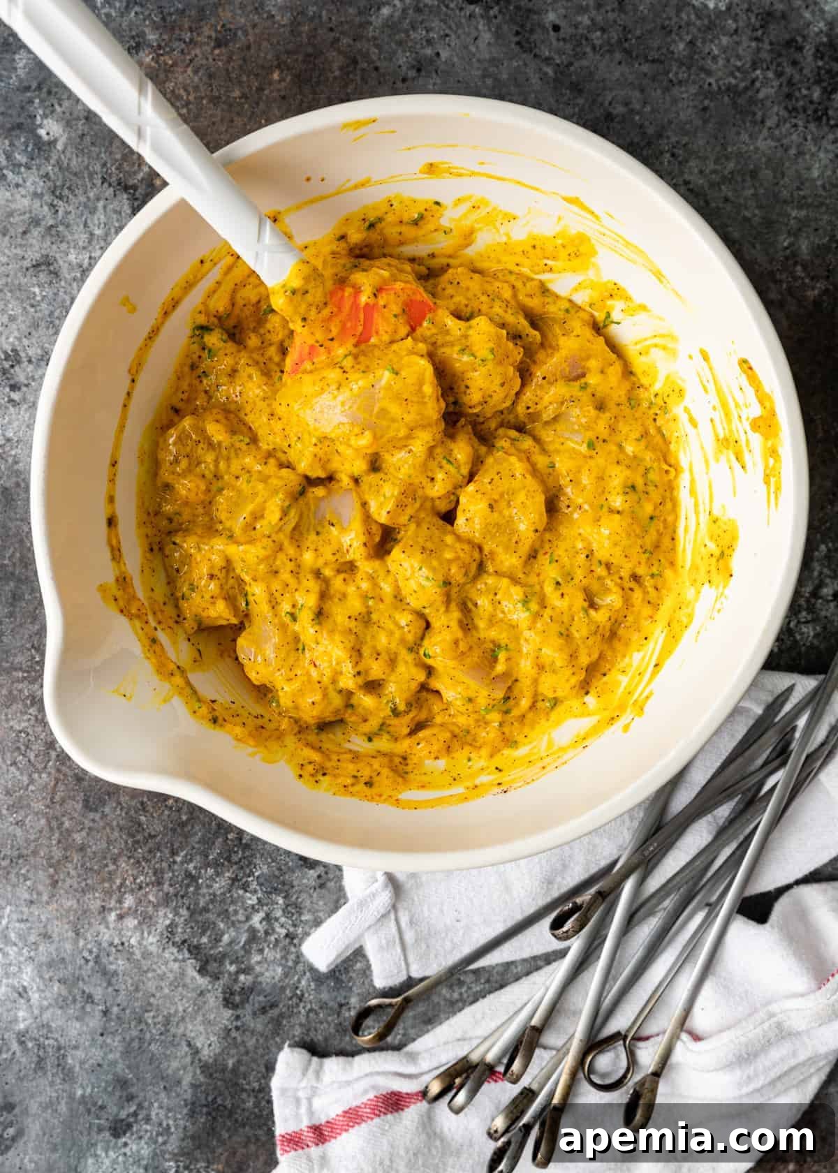 Overhead process shot demonstrating raw chicken breast cubes thoroughly marinating in a rich, saffron chicken kabob marinade, preparing for grilling.