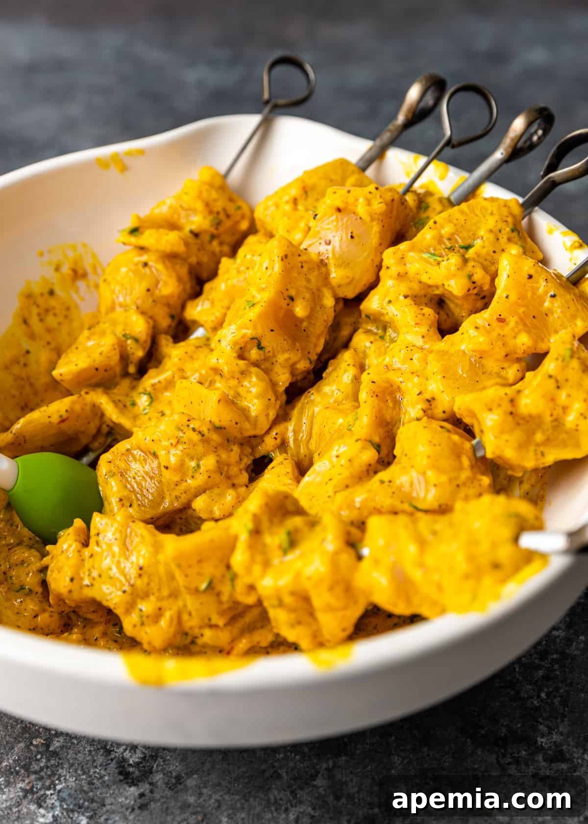 Raw, perfectly marinated pieces of saffron yogurt chicken expertly threaded onto metal kabob skewers, showcasing the vibrant color before cooking.