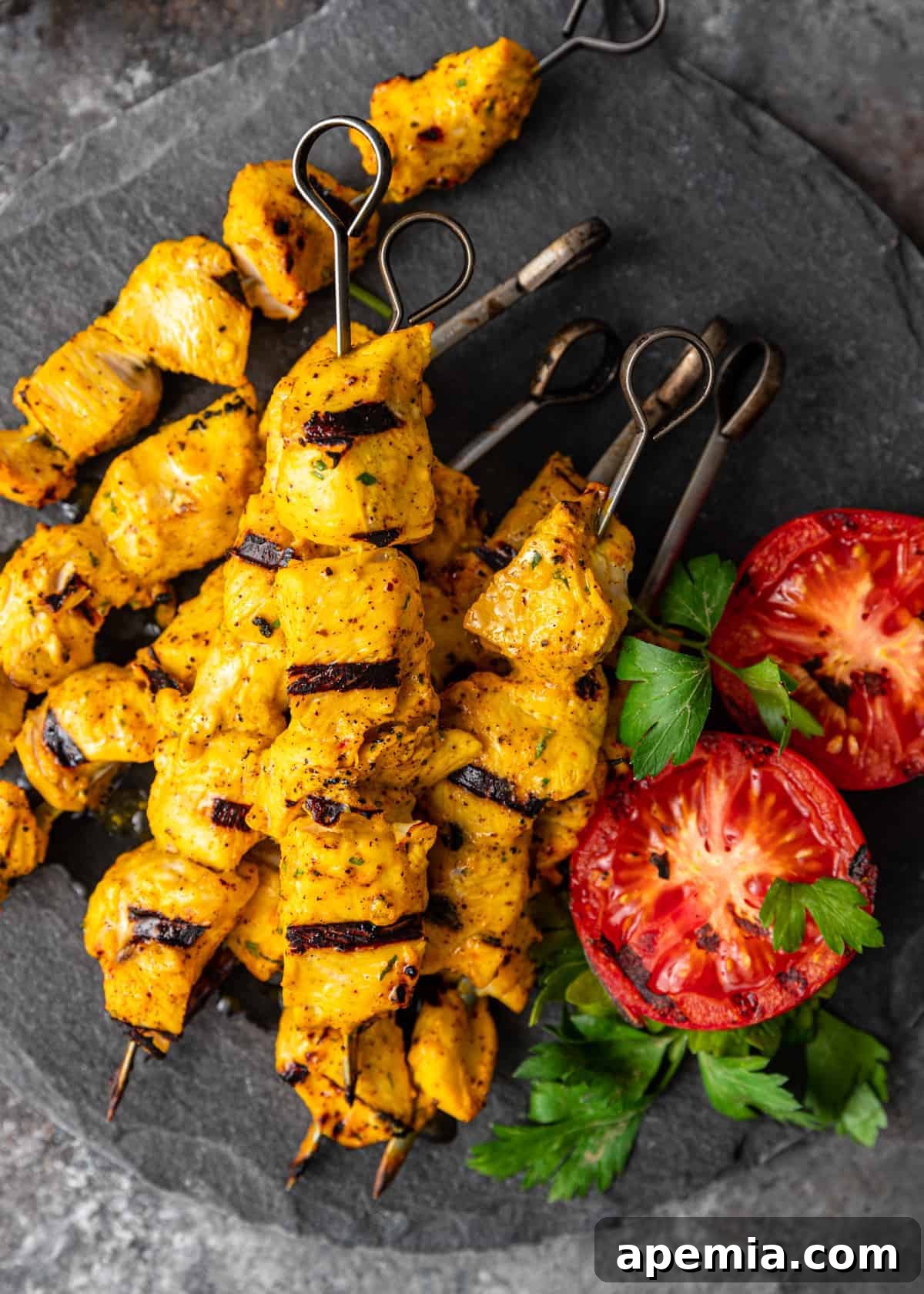 Overhead view of my Joojeh Kabob recipe presented on a sleek slate cutting board, accompanied by beautifully grilled tomatoes and a garnish of fresh herbs.