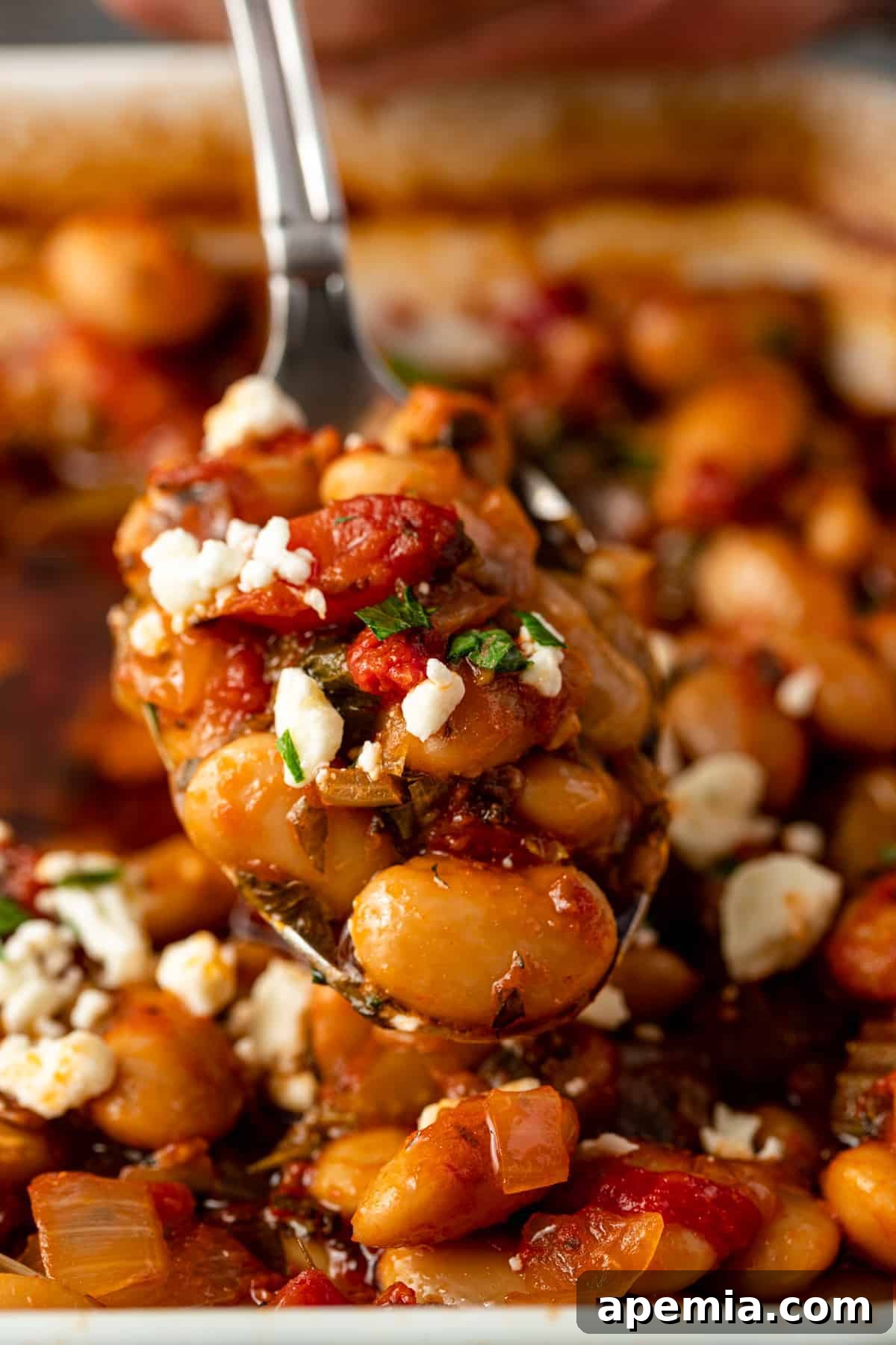closeup: spoonful of baked gigantes plaki topped with crumbled feta cheese