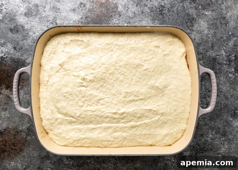 overhead process shot: layer of bechamel sauce in baking dish for greek lasagna
