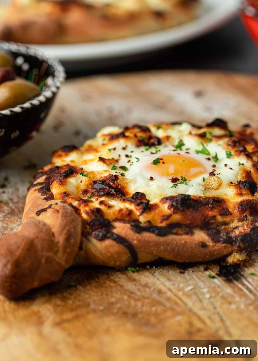 Georgia's Irresistible Khachapuri 3 A single boat-shaped Georgian Khachapuri cheese bread, golden brown and bubbling, on a wood serving board.