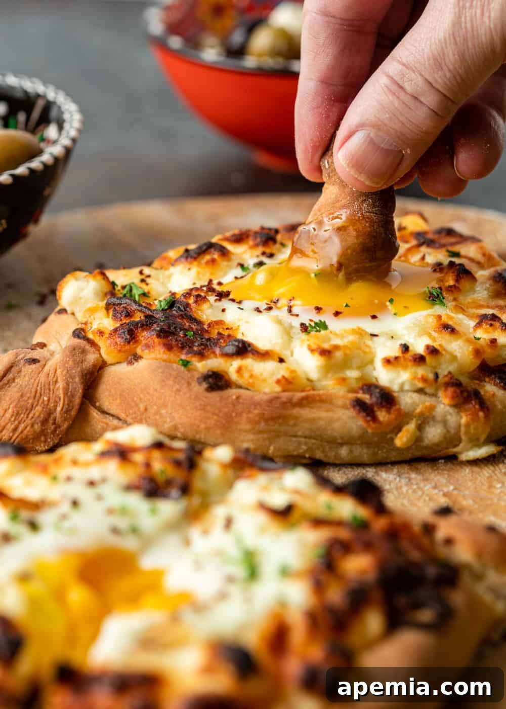 Georgia's Irresistible Khachapuri 5 A close-up shot of a piece of cheese bread being dipped into the rich, eggy center of a Georgian Khachapuri boat.