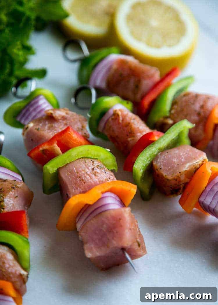 Closeup of skewers featuring boneless pork loin, vibrant red and green bell peppers, and red onion slices before grilling.