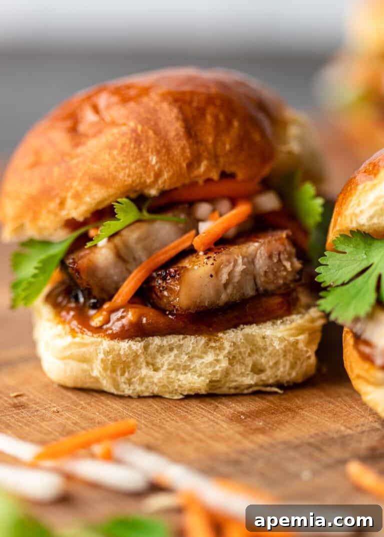 Close-up of a spicy pork belly slider on a soft bun, garnished with pickled carrots and fresh cilantro.